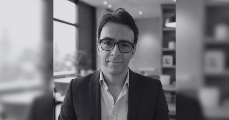 Portrait of a man wearing glasses and a dark blazer in an office setting, looking at the camera with a slight smile. - Terremotos, gasto público y reconstrucción