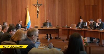 Government meeting in a wood-paneled room with officials around a long conference table; a crucifix and a Colombian flag on the wall. - Las2orillas.co: Historias, voces y noticias de Colombia