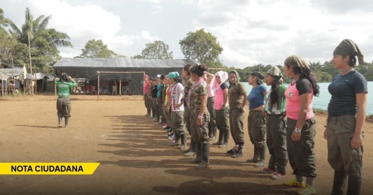 Line of women in cargo pants outdoors, standing at attention while a person in a green shirt leads a drill; a tent and trees in the background with a yellow 'NOTA CIUDADANA' banner in the corner. - La soledad de los padres colombianos cuyos hijos se fueron para las filas de la guerrilla