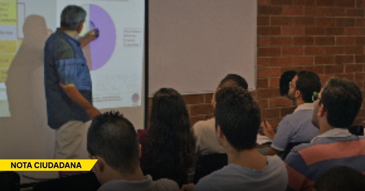 Lecturer in a blue shirt points at a projection screen with charts as a class watches. - Precarización y censura: las sombras que amenazan a los profesores universitarios