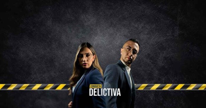 Así conquistaron dos periodistas colombianos el primer lugar de Spotify con historias de crimen Two professionals in formal attire stand back-to-back in front of a dark textured background with yellow caution tape, featuring the title 'Conducta Delictiva'. - Así conquistaron dos periodistas colombianos el primer lugar de Spotify con historias de crimen