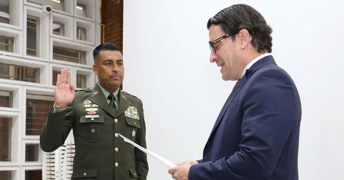 Army officer raises his right hand to take an oath as a civilian in a suit reads from a paper beside him, in a swearing-in ceremony. - El coronel que dirige el Inpec logró sostenerse en el cargo, ¿ cómo lo logro?