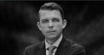 Black-and-white headshot of a man in a suit and tie, looking at the camera. - El camino es el correcto