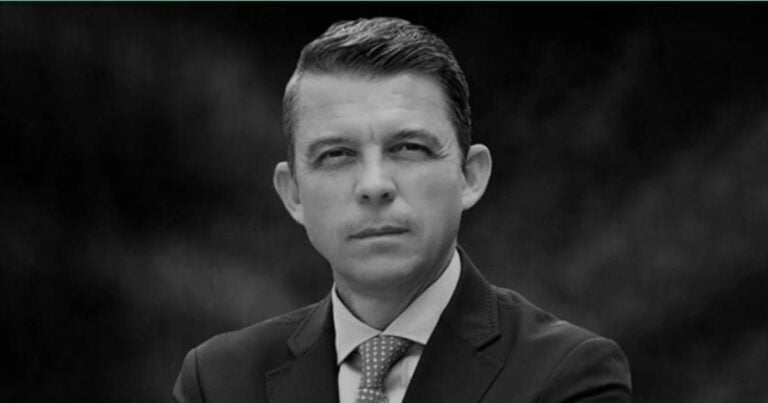 Black-and-white headshot of a man in a suit and tie, looking at the camera. - El camino es el correcto