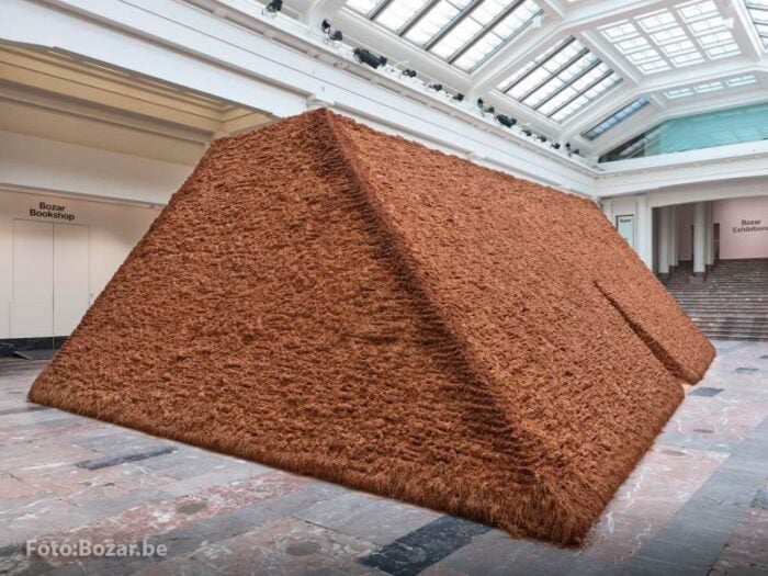 La cordobesa Delcy Morelos se despide del Palacio de Bellas Artes de Bruselas con una obra hecha con tierra de Bélgica Massive brown pyramid-shaped sculpture made of shaggy fibrous material in a museum atrium, surrounded by white walls and skylights. - La cordobesa Delcy Morelos se despide del Palacio de Bellas Artes de Bruselas con una obra hecha con tierra de Bélgica