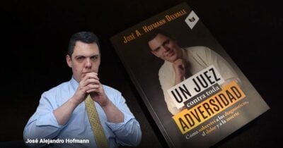 Man in a light blue shirt and yellow patterned tie sits with hands clasped; a tilted book cover beside him reads 'Un Juez contra toda Adversidad' (How to survive diagnoses and death). - La historia de José Alejandro Hofmann: el juez que convirtió la adversidad en un estrado de dignidad