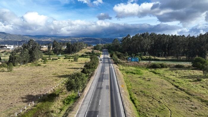 La obra que planeó Jorge Gaitán Cortés hace más de 60 años y continuó Peñalosa en el 98, por fin despega Straight two-lane road cuts through green fields toward distant hills under a cloudy sky, as seen from above. - La obra que planeó Jorge Gaitán Cortés hace más de 60 años y continuó Peñalosa en el 98, por fin despega