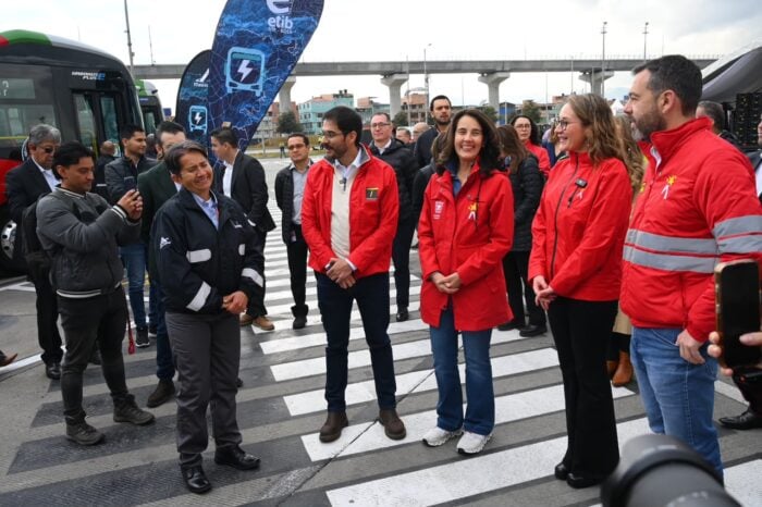 Los chinos en asocio con fabricantes de carrocerías caleños y brasileños hicieron 50 buses duales de Transmilenio Group of people wearing red event jackets standing on a crosswalk at an outdoor event, near a bus and banner. - Los chinos en asocio con fabricantes de carrocerías caleños y brasileños hicieron 50 buses duales de Transmilenio