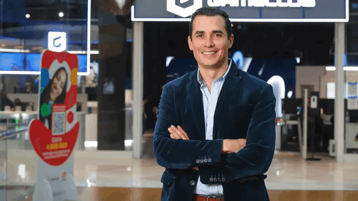 Con un billón de pesos la familia chilena Solari le compró 9 centros a la paisa Argos y Conconcreto Professional man in a navy blazer stands with arms crossed in a bright, modern showroom, smiling at the camera. - Con un billón de pesos la familia chilena Solari le compró 9 centros a la paisa Argos y Conconcreto