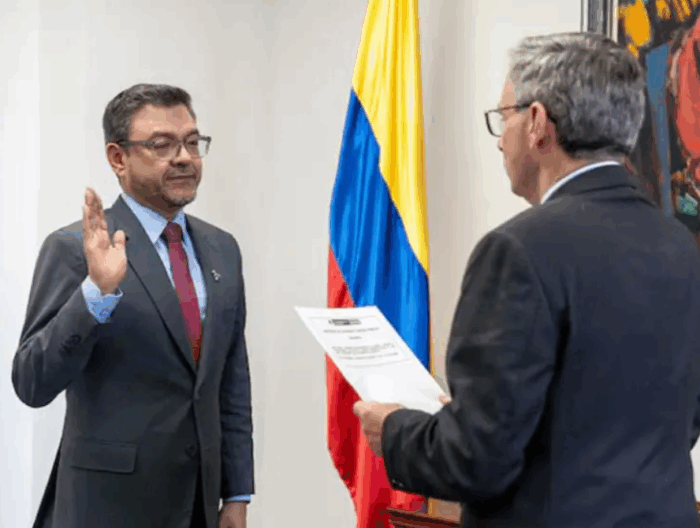 Con Viviane Morales al frente, los cristianos aterrizan con cargos de poder en el Ministerio de Educación Two men in suits participate in a formal oath ceremony; one raises his right hand as the other hands a certificate, with a Colombian flag in the background. - Con Viviane Morales al frente, los cristianos aterrizan con cargos de poder en el Ministerio de Educación