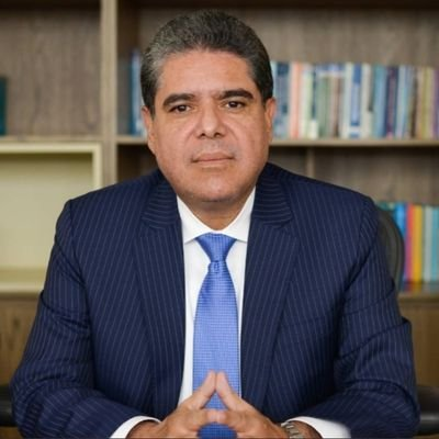 Anes de irse, el contralor Carlos Hernán Rodríguez sacó a 341 funcionarios que vigilaban la corrupción en las regalías Portrait of a middle-aged man in a dark pinstripe suit and blue tie, seated at a desk with bookshelves behind him. - Anes de irse, el contralor Carlos Hernán Rodríguez sacó a 341 funcionarios que vigilaban la corrupción en las regalías