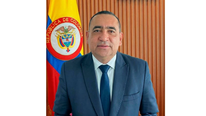 Un piloto con 30 años de experiencia en la FAC toma las riendas de la Aeronáutica en medio de una de sus peores crisis Man in a navy suit and blue tie poses indoors with the Colombian flag in the background. - Un piloto con 30 años de experiencia en la FAC toma las riendas de la Aeronáutica en medio de una de sus peores crisis