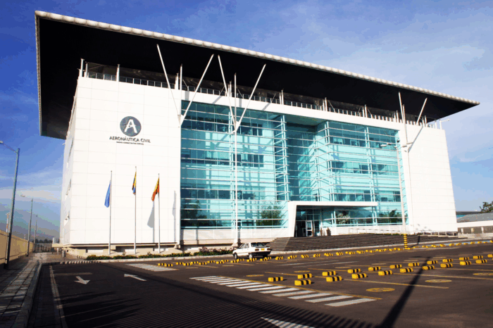 Un piloto con 30 años de experiencia en la FAC toma las riendas de la Aeronáutica en medio de una de sus peores crisis Front view of a modern aviation authority building with a glass façade, white walls, and a large 'A' logo reading Aeronáutica Civil, flags outside, and a parking area in front. - Un piloto con 30 años de experiencia en la FAC toma las riendas de la Aeronáutica en medio de una de sus peores crisis