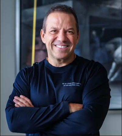 Smiling man with arms crossed, wearing a dark navy shirt, standing in a modern indoor setting. - Un millonario pleito por fraude persigue en Nueva York al empresario y excandidato Santiago Botero