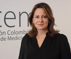 Portrait of a professional woman with shoulder-length brown hair, wearing a black blouse, standing in front of a light backdrop with partial text. - Un equipo formado mayoritariamente por mujeres inicia la tarea de recuperar el sistema de salud