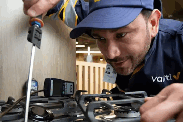 La fórmula del presidente de Vanti para asegurar que no habrá escasez de gas Gas cooktop repair technician tightening a burner with a screwdriver, wearing a navy uniform and cap with a Vatti logo in a workshop - La fórmula del presidente de Vanti para asegurar que no habrá escasez de gas