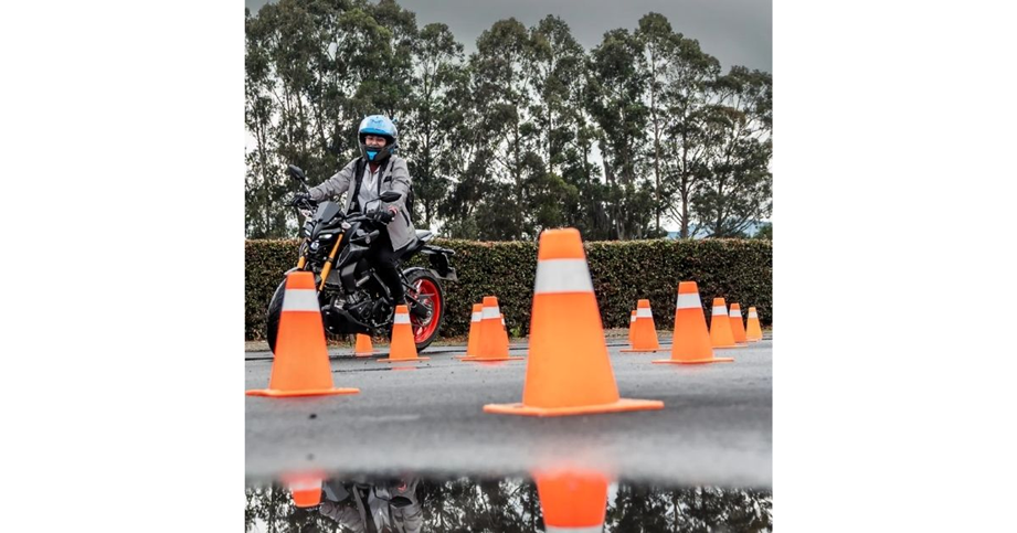 Yamaha sacó del trancón a 250 motociclistas y los puso a correr en el Autódromo de Tocancipá Motorcyclist wearing helmet and jacket navigates a cone slalom on a wet parking lot, with a reflection in the water nearby. - Yamaha sacó del trancón a 250 motociclistas y los puso a correr en el Autódromo de Tocancipá