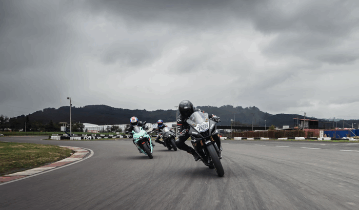Yamaha sacó del trancón a 250 motociclistas y los puso a correr en el Autódromo de Tocancipá Three motorcyclists lean into a turn on a race track under cloudy skies and hills in the distance. - Yamaha sacó del trancón a 250 motociclistas y los puso a correr en el Autódromo de Tocancipá