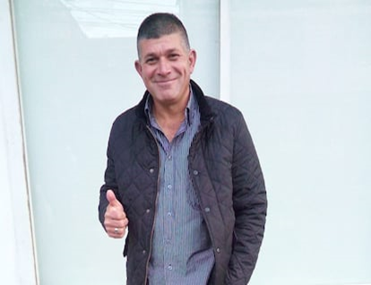 Lo condenaron por matar a Álvaro Gómez, pasó 18 años preso y hoy las Farc dicen que es inocente Smiling man in a dark quilted jacket giving a thumbs-up, standing against a light glass wall. - Lo condenaron por matar a Álvaro Gómez, pasó 18 años preso y hoy las Farc dicen que es inocente