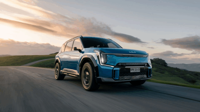 La camioneta eléctrica de Kia que parece sacada del futuro: seis pasajeros, potente y con casi 500 km de autonomía Blue SUV driving on a scenic mountain road at sunset (front-left angle) - La camioneta eléctrica de Kia que parece sacada del futuro: seis pasajeros, potente y con casi 500 km de autonomía