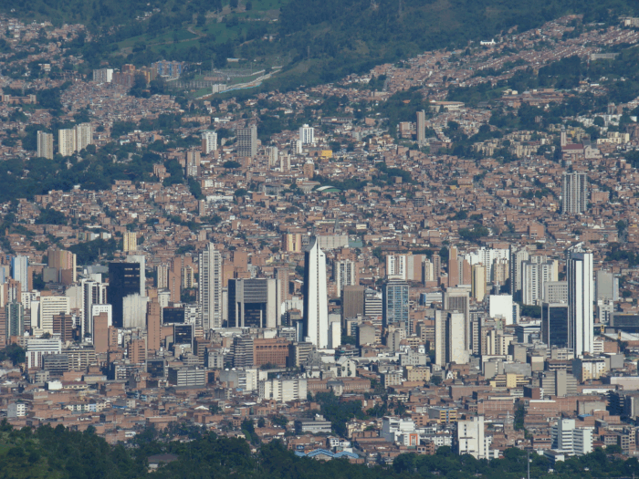 El salto de Claudia Carrasquilla: de concejal de Medellín a viceministra de Defensa Wide view of a densely built hillside city with brown residential buildings and several tall office towers, set against green hills in the distance. - El salto de Claudia Carrasquilla: de concejal de Medellín a viceministra de Defensa