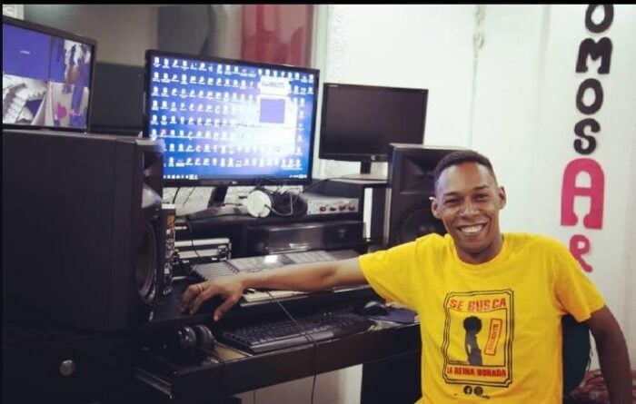 Don Rey, el músico de Quibdó que cambió las armas por instrumentos a cientos de jóvenes del Chocó Smiling man in a yellow t‑shirt seated at a mixing console in a recording studio with computer monitors and speakers. - Don Rey, el músico de Quibdó que cambió las armas por instrumentos a cientos de jóvenes del Chocó