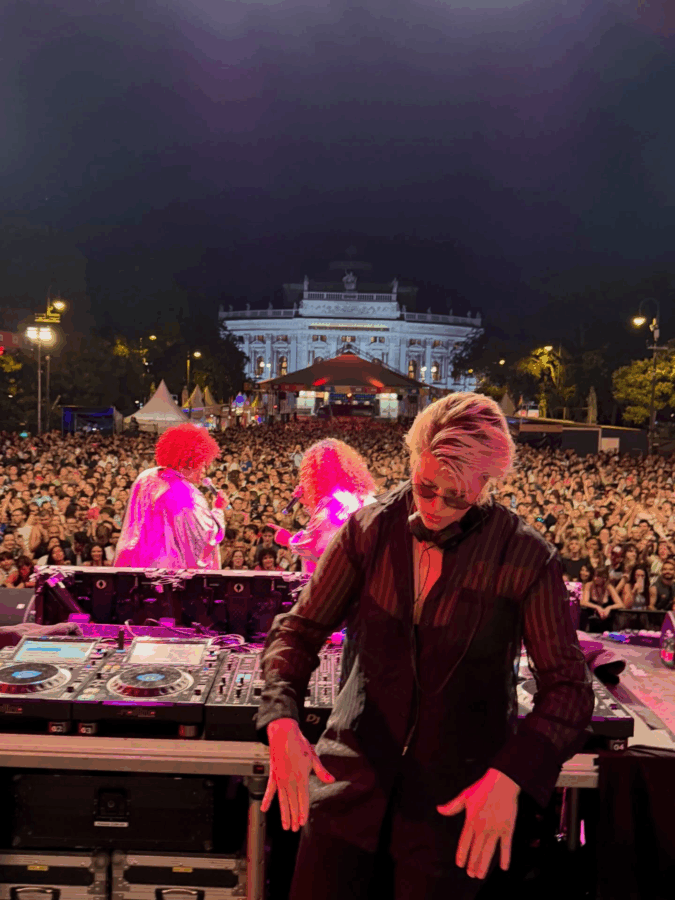 Gunn Lundemo, la DJ que terminó convirtiéndose en una de las amigas más cercanas de Verónica Alcocer DJ performing on a night-lit stage with a large cheering crowd and a grand, illuminated building in the background on a city square. - Gunn Lundemo, la DJ que terminó convirtiéndose en una de las amigas más cercanas de Verónica Alcocer