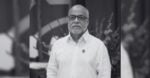 Portrait of an older man with glasses and a white button-down shirt, standing outdoors with blurred plants in the background. - EMPLEO: Será verdad que estamos tan bien? cambiemos hacia una actitud de servicios.