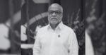 Portrait of a bald man with glasses and a white button-down shirt, standing outdoors with a badge on his chest - El Caribe también es café