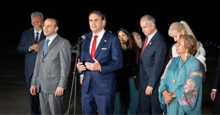 Así fue la llegada a Cali de presidentes e invitados especiales a la posesión de Abelardo De la Espriella Man in a navy suit and red tie speaks into a microphone at a nighttime press event, surrounded by suited colleagues. - Así fue la llegada a Cali de presidentes e invitados especiales a la posesión de Abelardo De la Espriella