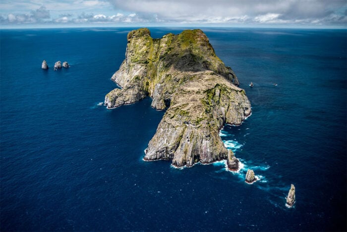 Tras 20 años dedicada a salvar una isla remota del Pacífico, la bióloga Sandra Bessudo cuidará los 65 Parques Nacionales Aerial view of a rugged rocky island rising from deep blue ocean with smaller rocks nearby under a cloudy sky. - Tras 20 años dedicada a salvar una isla remota del Pacífico, la bióloga Sandra Bessudo cuidará los 65 Parques Nacionales