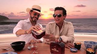 Una barranquillera que suma la cercanía de su papá el petrolero Federico Restrepo con el presidente, será vicecanciller Two smiling men on a boat at sunset toast with drinks, one wearing a straw hat and the other in sunglasses. - Una barranquillera que suma la cercanía de su papá el petrolero Federico Restrepo con el presidente, será vicecanciller