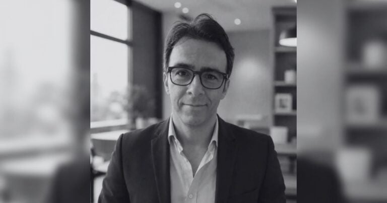 Professional grayscale portrait: man wearing glasses and a blazer in an office setting, looking at the camera. - Más allá de la mampostería