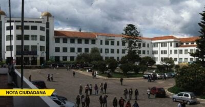 Wide view of a campus quad with white university buildings, students walking, and parked cars under a cloudy sky. - Las2orillas.co: Historias, voces y noticias de Colombia