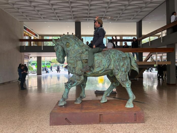 Cuando París, hace 50 años, fue el semillero de 29 grandes artistas colombianos Man riding a large bronze horse statue inside a museum lobby, with onlookers and a balcony above. - Cuando París, hace 50 años, fue el semillero de 29 grandes artistas colombianos