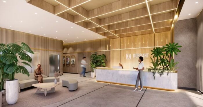 La reaparición de Andrés Camargo con un proyecto que sorprenderá en Bogotá Modern hotel lobby with a marble reception desk, gold-accent decor, and large potted plants; a guest approaches while staff assist nearby. - La reaparición de Andrés Camargo con un proyecto que sorprenderá en Bogotá