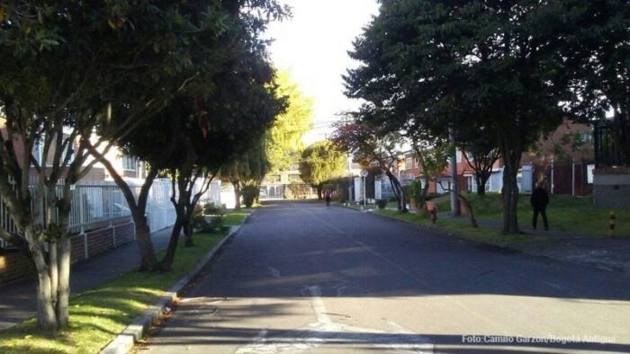 La antigua Hacienda Niza de la familia hurtado en Bogotá termino dando el nombre al barrio Niza de Suba. Quiet residential street lined with trees on both sides, a sidewalk, and a few pedestrians in the distance on a sunny day. - La antigua Hacienda Niza de la familia hurtado en Bogotá termino dando el nombre al barrio Niza de Suba.