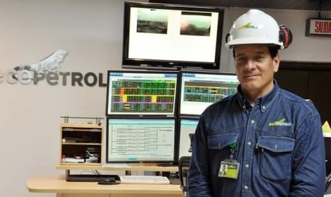 Cuatro petroleras están listas a la espera de que De la Espriella le de largada al fracking Male technician in a blue work shirt and white hard hat stands in a control room with multiple monitors displaying data; Ecopetrol logo on the wall. - Cuatro petroleras están listas a la espera de que De la Espriella le de largada al fracking