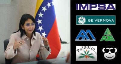 Las2orillas.co: Historias, voces y noticias de Colombia Woman in a light blazer speaks at a desk during a meeting, with a Venezuelan flag in the background. On the right is a column of company logos (IMPSA, GE Vernova, Andinalmas & Andimetales, AJE, Palnotres, panda logo). - Las2orillas.co: Historias, voces y noticias de Colombia