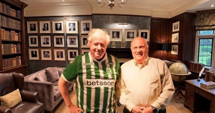 El poder del ex presidente Iván Duque con su Fundación que trajo al ex ministro Boris Johnson a Colombia Two men stand together in a wood-paneled study, one in a green striped Betsson jersey and the other in a light shirt, with framed portraits on the wall behind them. - El poder del ex presidente Iván Duque con su Fundación que trajo al ex ministro Boris Johnson a Colombia