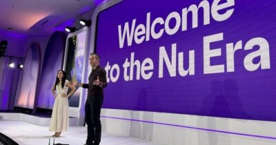 Las2orillas.co: Historias, voces y noticias de Colombia Two presenters on a stage in front of a large purple screen reading 'Welcome to the Nu Era'. - Las2orillas.co: Historias, voces y noticias de Colombia