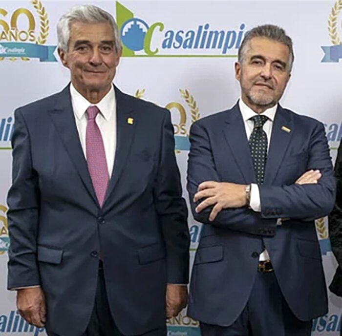 Una empresa digital de aseo de hogares y oficinas le ha ido ganando terreno a la tradicional Casa Limpia Two men in dark suits posing for a photo at a formal event, standing before a branded backdrop reading Casalimpi/related logos. - Una empresa digital de aseo de hogares y oficinas le ha ido ganando terreno a la tradicional Casa Limpia