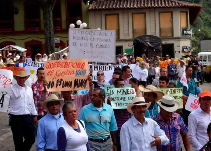 La apuesta de Alberto Calderón como cabeza de AngloGold Ashanti con la mina de cobre de Quebradona en Jericó Crowd of protesters in a town square, many wearing hats, carrying handmade signs in Spanish about water, mining, and the environment. - La apuesta de Alberto Calderón como cabeza de AngloGold Ashanti con la mina de cobre de Quebradona en Jericó