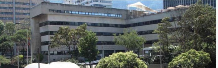 Concrete office building with horizontal windows, flanked by trees in a sunny urban campus setting. - La Empresa de Acueducto de Bogotá busca el permiso de Minambiente para reutilizar las aguas residuales en industria
