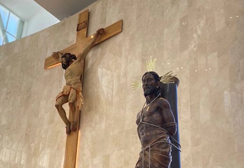 El terrible secreto que escondía el cementerio donde están enterrados Diomedes Díaz, Escalona y Martín Elías Wooden crucifix with Jesus on the cross beside a bound man statue with a halo on a marble church wall. - El terrible secreto que escondía el cementerio donde están enterrados Diomedes Díaz, Escalona y Martín Elías