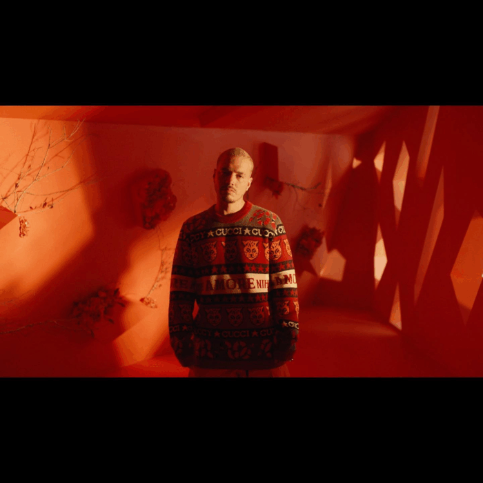 El paisa que terminó detrás de Cien años de soledad y trabajando con J Balvin, Feid y Juanes Man wearing a Gucci-pattern sweater stands in a red-lit room with angular wall shadows behind him. - El paisa que terminó detrás de Cien años de soledad y trabajando con J Balvin, Feid y Juanes
