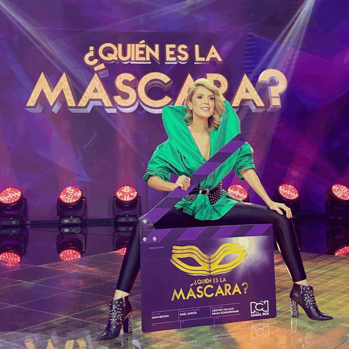 Alejandra Azcárate está lista para volver a la televisión de la mano de Netflix, Caracol y Dago García Woman in a bright green outfit posing on a large purple clapperboard prop on a TV stage, with 'Quién es la máscara?' in the background. - Alejandra Azcárate está lista para volver a la televisión de la mano de Netflix, Caracol y Dago García