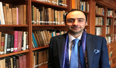 El regreso de Alejandro Ordoñez a la vida pública de Colombia con más poder que nunca en la era del Tigre Man in a dark suit and blue tie stands in a library with tall wooden shelves filled with books behind him. - El regreso de Alejandro Ordoñez a la vida pública de Colombia con más poder que nunca en la era del Tigre
