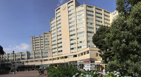 La coronel médica que se estrena como directora del Hospital Militar hereda una dura multa por un contrato que no firmó Large beige multi-story hospital building with glass entrance, blue sky, and an ambulance parked in front near trees on the right. - La coronel médica que se estrena como directora del Hospital Militar hereda una dura multa por un contrato que no firmó