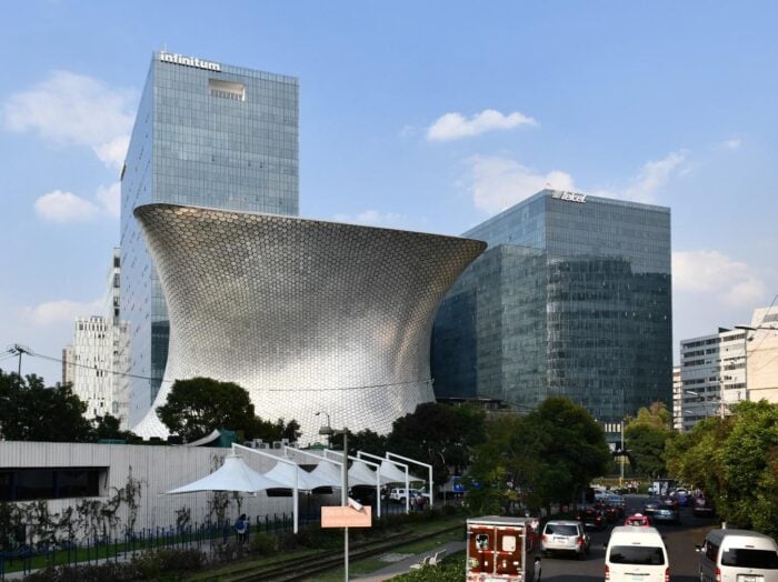 Los negocios que llevaron a la cima a los cinco más ricos de América Latina entre los que hay un colombiano Silver, hourglass-shaped building with a honeycomb metal facade beside glass office towers in a busy city street scene (Museo Soumaya, Mexico City). - Los negocios que llevaron a la cima a los cinco más ricos de América Latina entre los que hay un colombiano